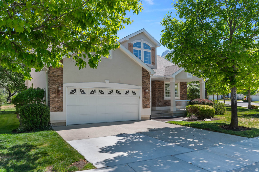 Two-story residence featuring a stone and stucco exterior, an attached two-car garage with decorative windows, and a covered front porch with white columns