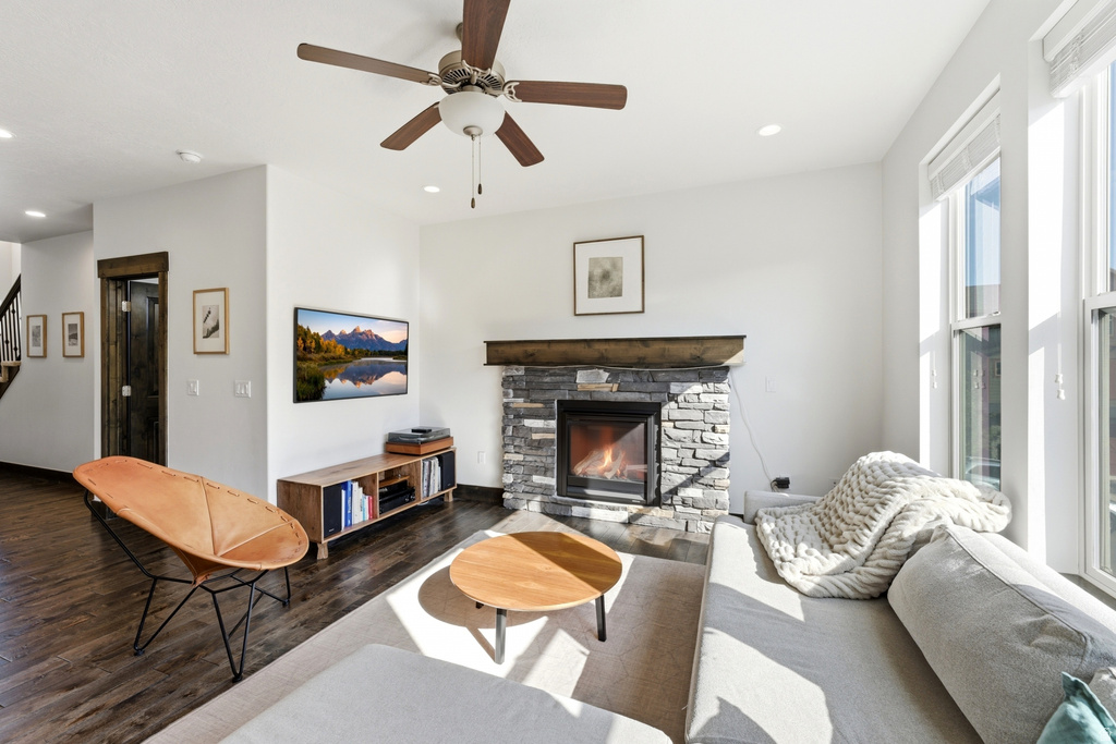 Living area featuring a stone fireplace with a wood mantle, wood-finish flooring, a ceiling fan, recessed lighting, and multiple windows