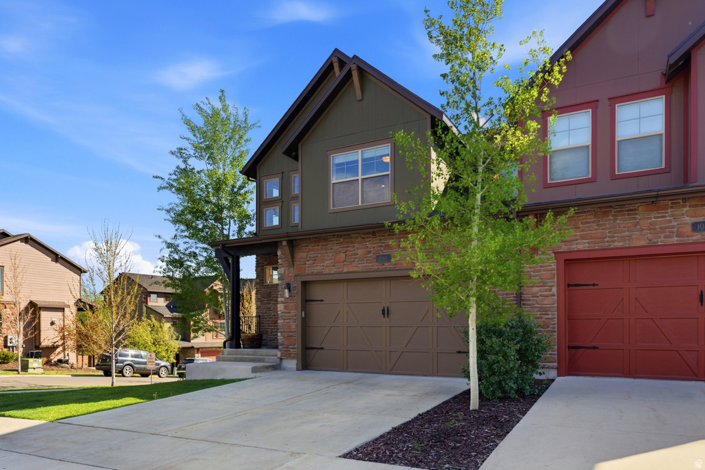 Contemporary townhome exterior featuring an attached garage, concrete driveway, and mature landscaping