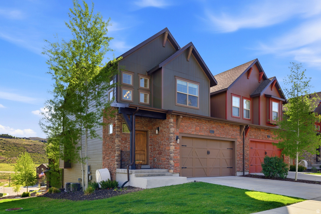 Modern townhouse exterior featuring a warm wood entry door, stone veneer facade, integrated two-car garage, and a verdant lawn