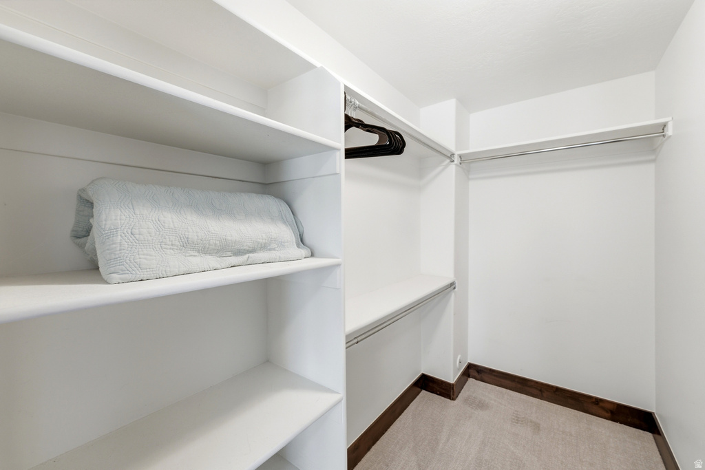 Walk-in closet featuring built-in shelving, chrome hanging rods, and light-toned carpeting with a dark wood baseboard