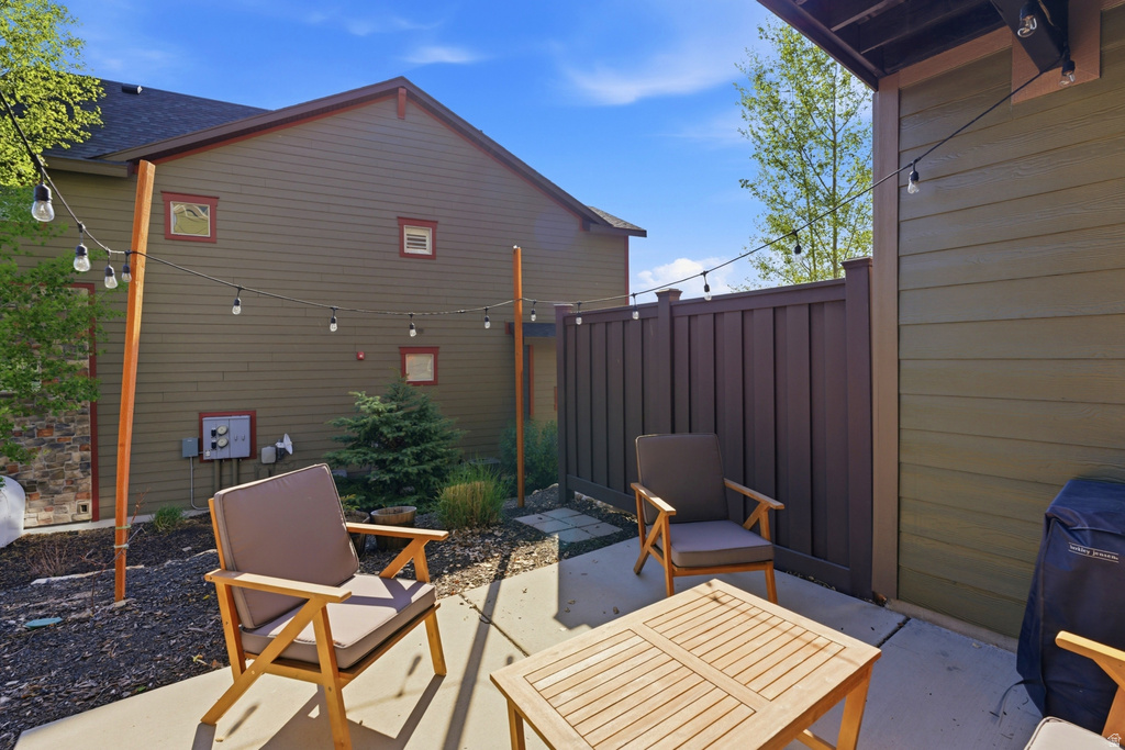 Concrete patio featuring a privacy fence, string lighting, and mature landscaping
