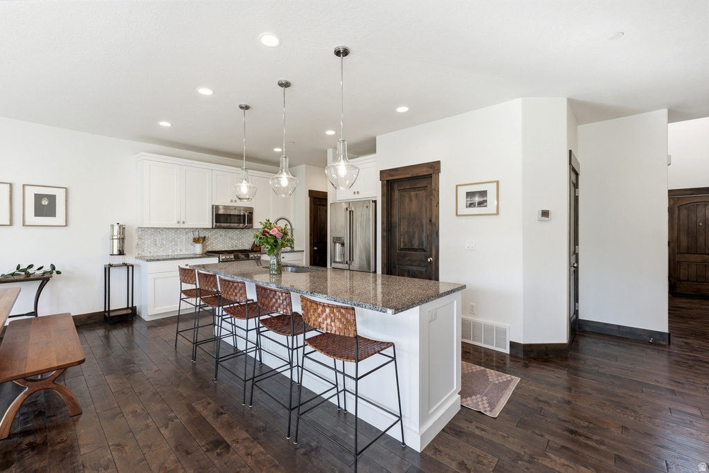 Spacious kitchen featuring an expansive center island with seating, white cabinetry, granite countertops, and stainless steel appliances