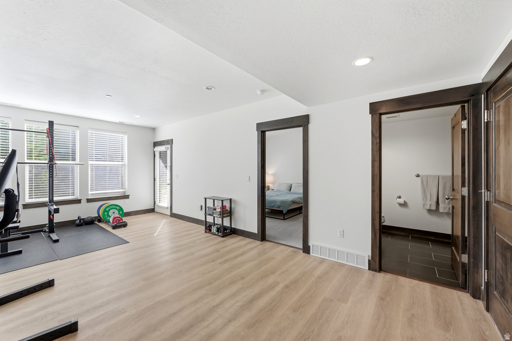Spacious room with light wood-finish flooring and multiple windows with blinds