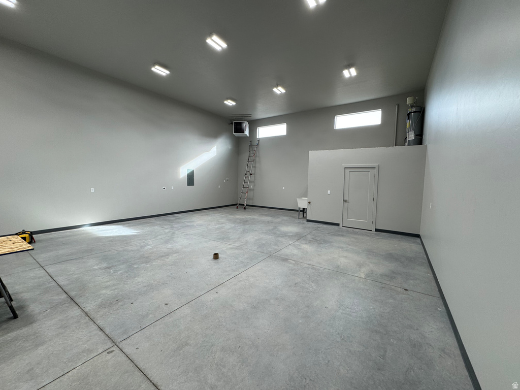 Expansive open-concept space featuring concrete flooring, a neutral color palette, multiple ceiling-mounted light fixtures, transom windows, and a utility sink