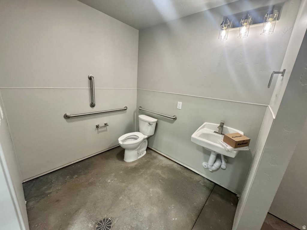 Restroom featuring a wall-mounted toilet, wall-mounted sink, three chrome grab bars, and a three-light vanity fixture