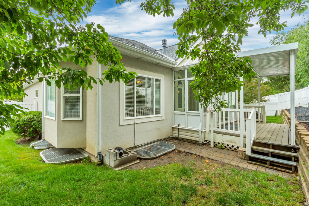 Rear exterior featuring a sunroom, an attached deck with a covered patio, and manicured green space