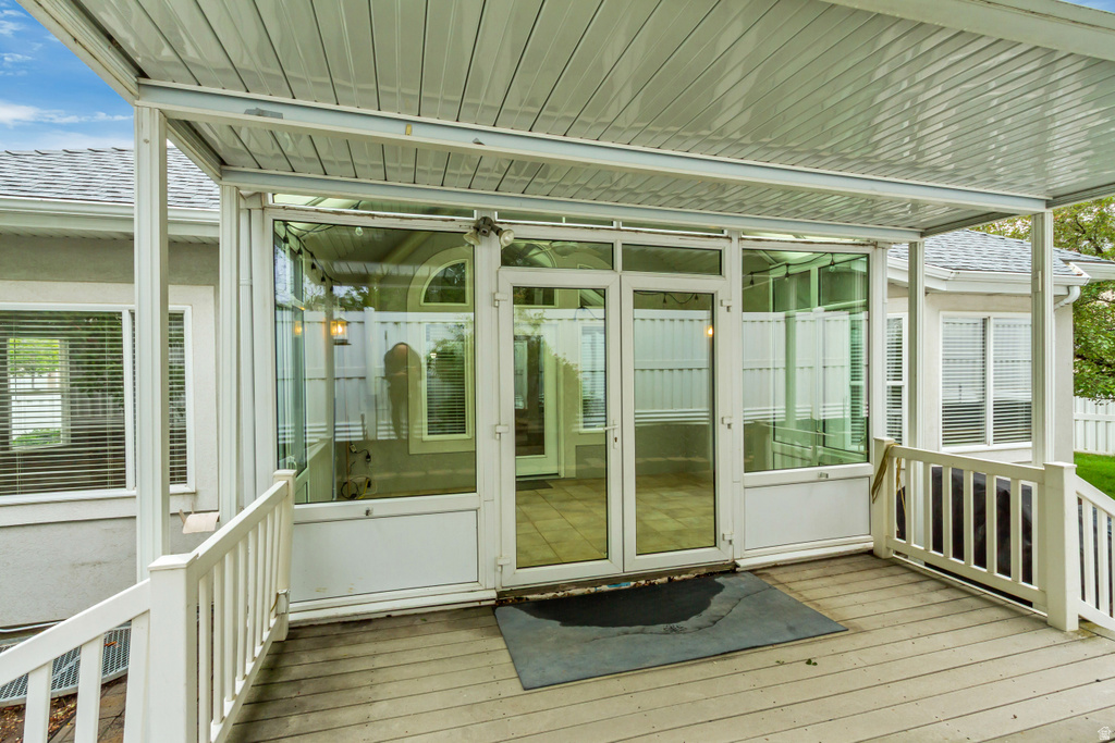 Covered outdoor deck with white railing and direct access to a glass-enclosed room featuring a vaulted ceiling and an arched transom window