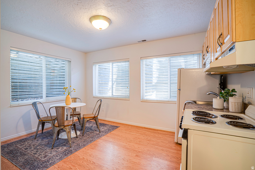 Efficient kitchen space featuring wood-finish flooring, light wood cabinetry with dark hardware, a four-burner electric range, a stainless steel sink, and multiple windows with horizontal blinds