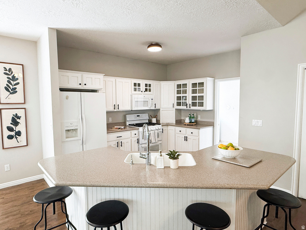 White cabinetry, corner sink, built-in breakfast bar, wood-finish flooring, and recessed lighting
