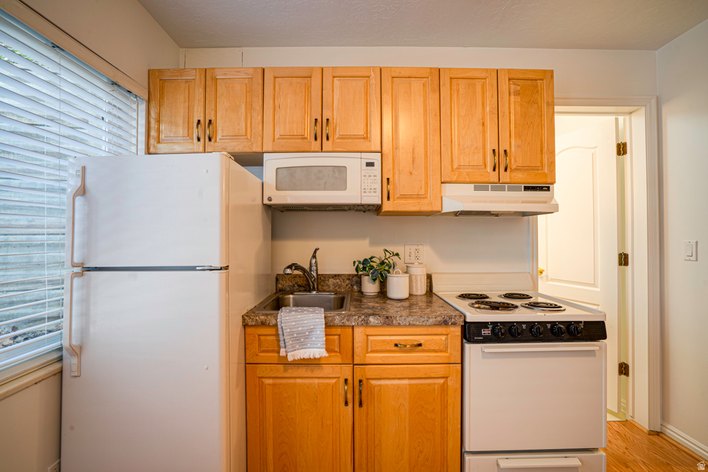 Compact kitchen featuring light wood cabinetry, stone-finish countertops, and a white appliance suite including a refrigerator, range, and microwave