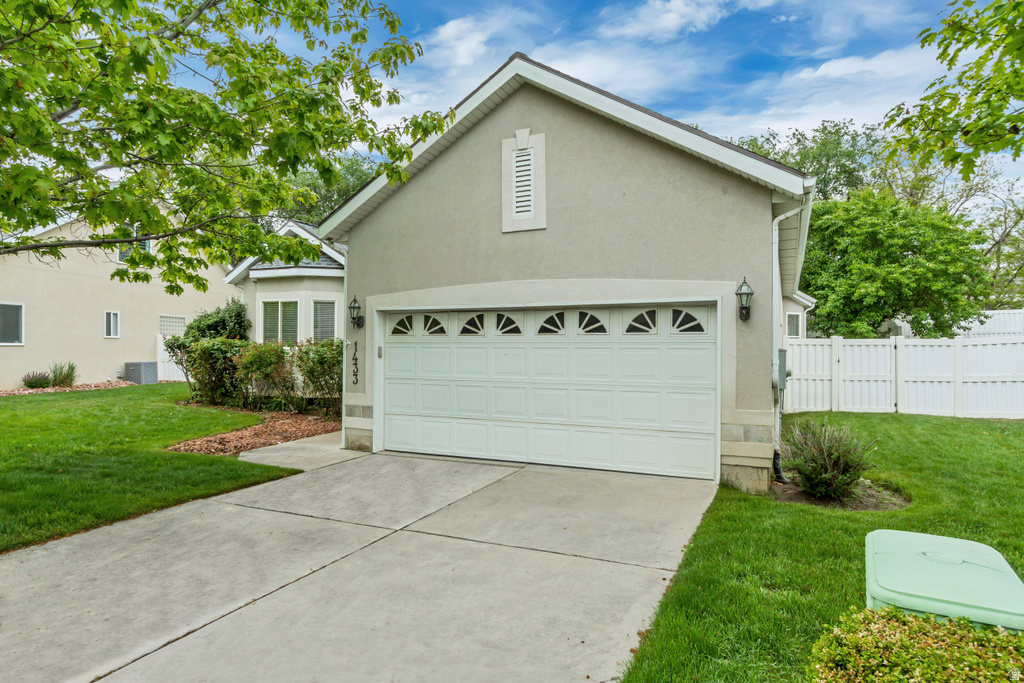 Stucco-sided residence featuring an attached garage with decorative windows, a concrete driveway, and a manicured lawn