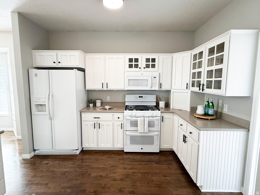 White cabinetry with dark hardware, built-in microwave, white refrigerator, gas range with double oven, and wood-finish flooring
