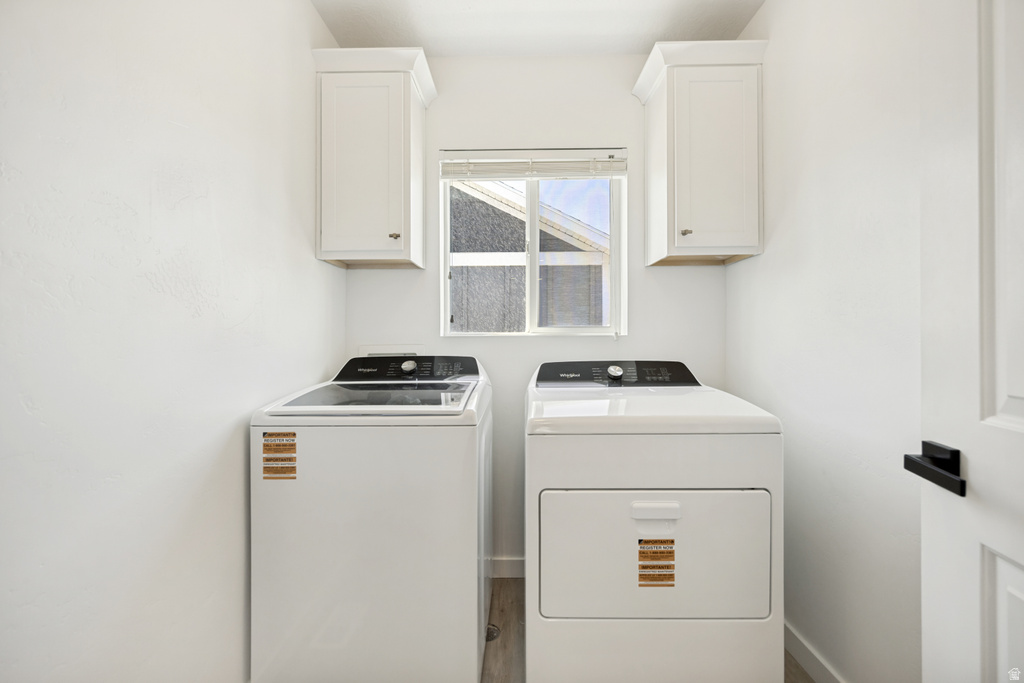 Dedicated laundry area with a window, two upper white shaker-style cabinets, and wood-finish flooring