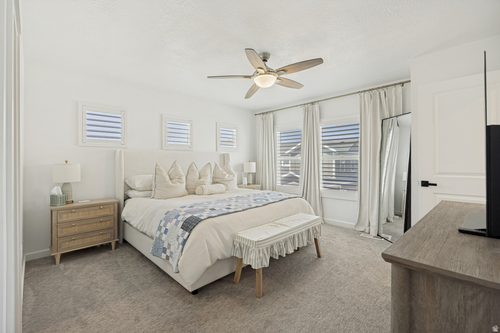 Carpeted bedroom featuring white walls, a ceiling fan with integrated lighting, and multiple windows with horizontal blinds and drapery
