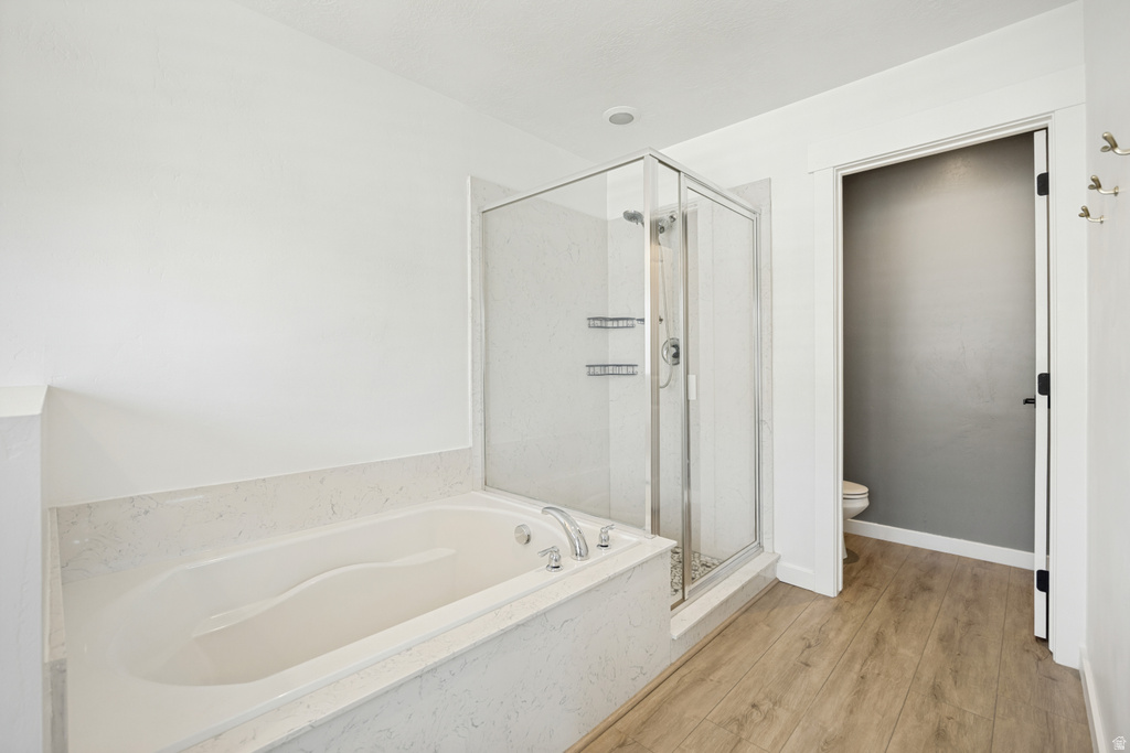 Soaking tub with a light-toned surround, frameless glass shower enclosure, and wood-finish flooring