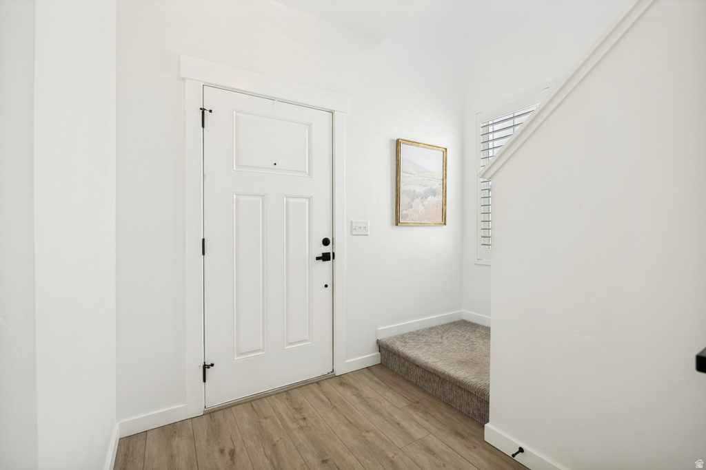 Entryway featuring a white paneled door with matte black hardware, wood-finish flooring, and a carpeted staircase