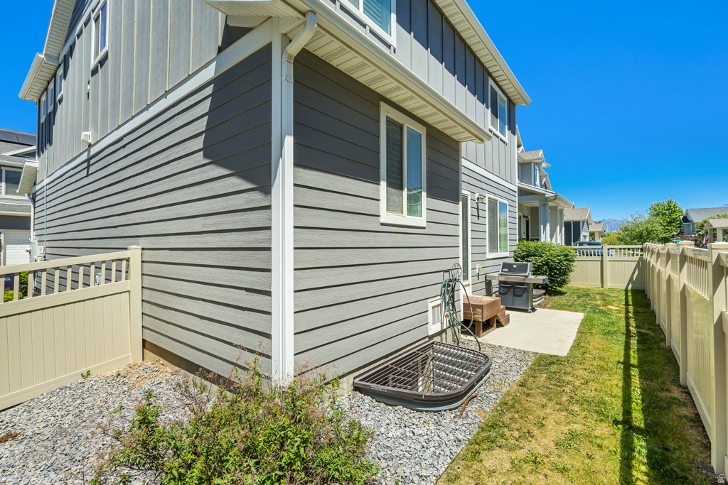 Exterior featuring horizontal gray siding, white trim, multiple windows, a concrete patio, and a light-colored privacy fence