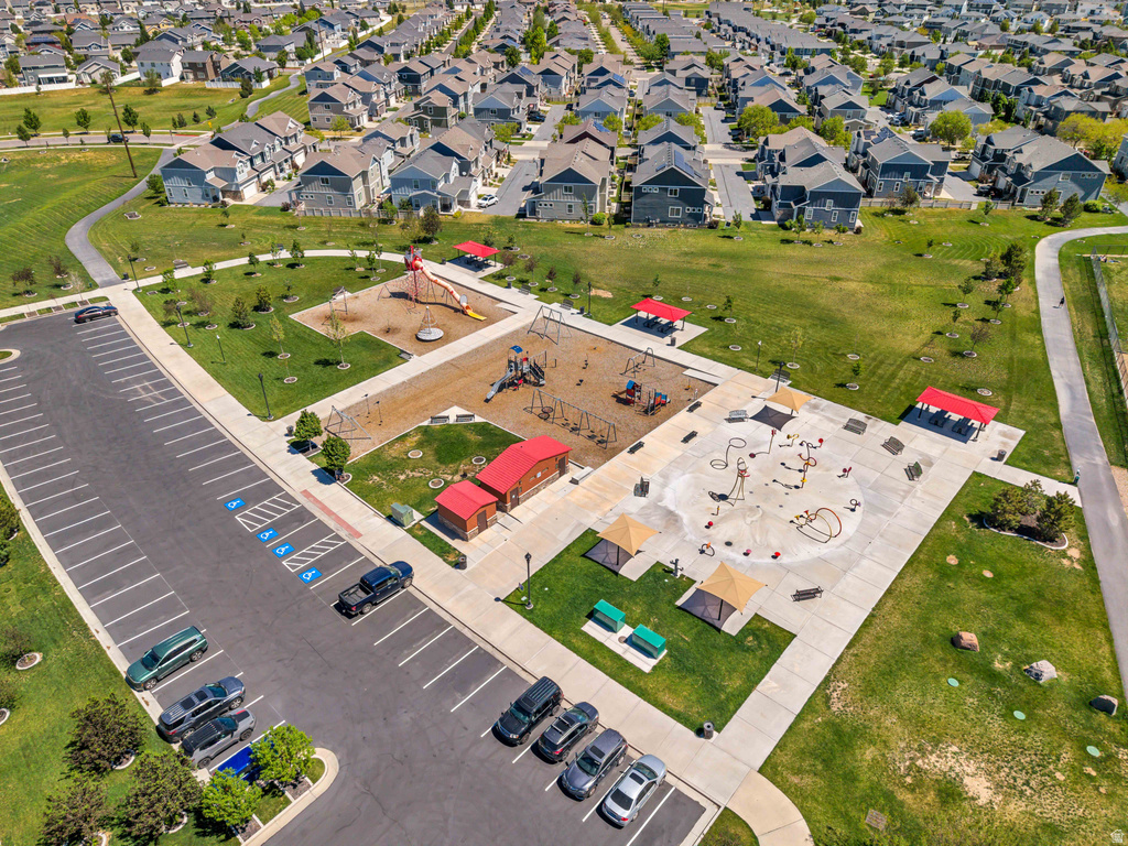 Community park featuring a splash pad, multiple play structures, covered seating areas, and a paved parking lot
