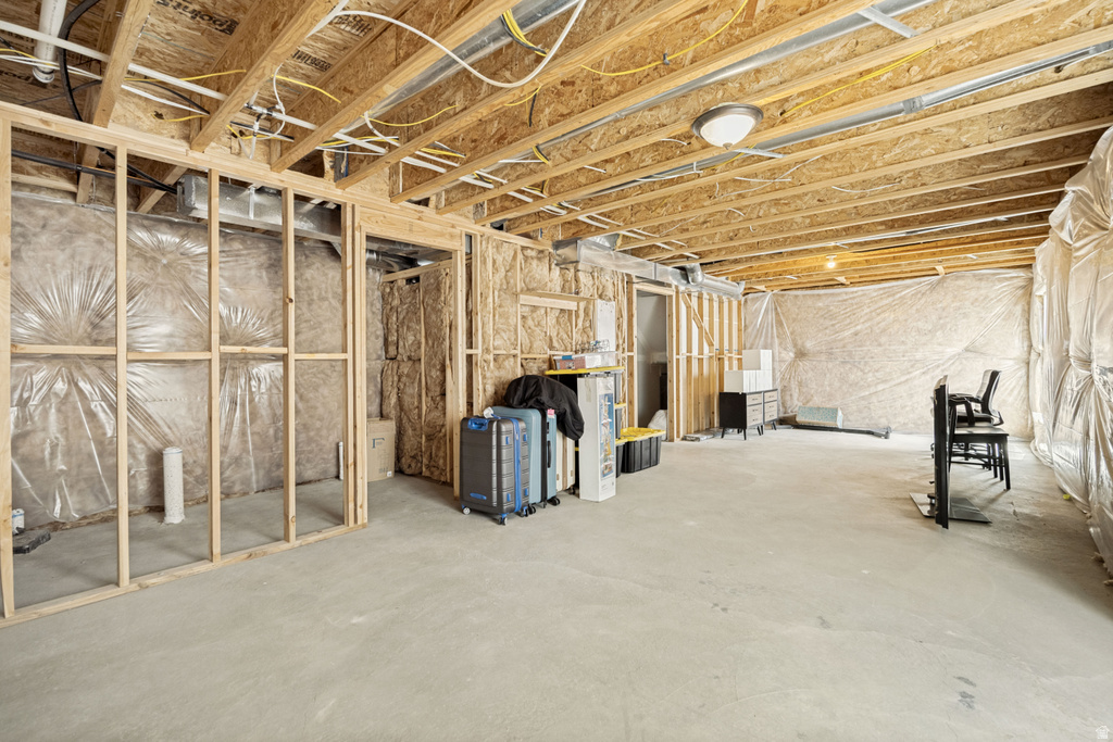 Unfinished basement featuring concrete flooring, exposed wood ceiling joists, framed wall partitions, a ceiling-mounted light fixture, and insulation-lined perimeter walls
