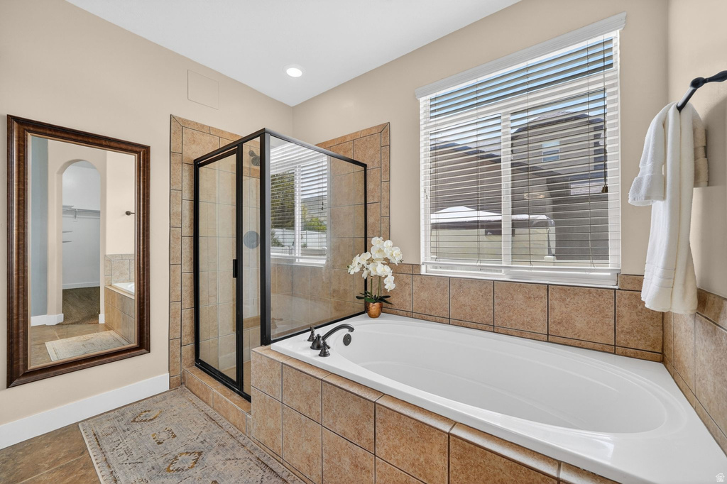 Bathroom featuring a tiled soaking tub with deck-mounted fixtures, a glass-enclosed shower with a black frame, and neutral wall tile