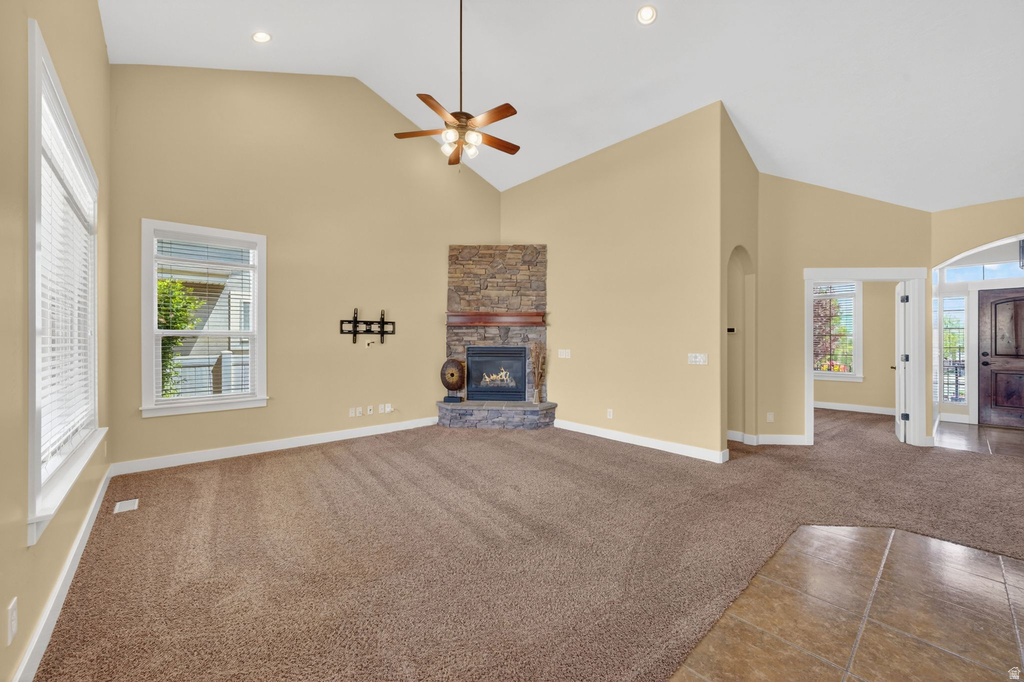 Spacious living area featuring a vaulted ceiling with a ceiling fan, a stone-faced fireplace, large windows with blinds, and carpet flooring