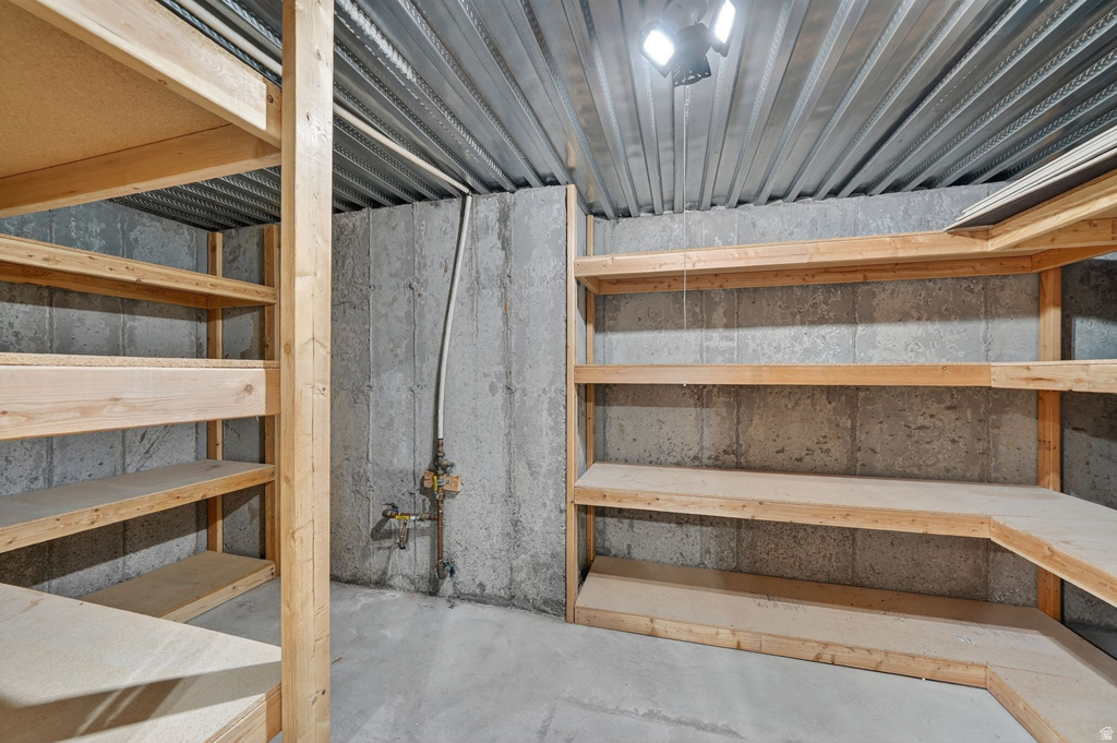 Concrete walled storage area featuring extensive built-in wooden shelving, a corrugated metal ceiling, and overhead lighting