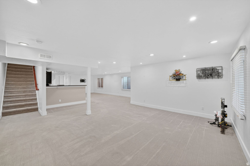 Spacious carpeted room featuring recessed lighting, a built-in bar, and a staircase with wood railing