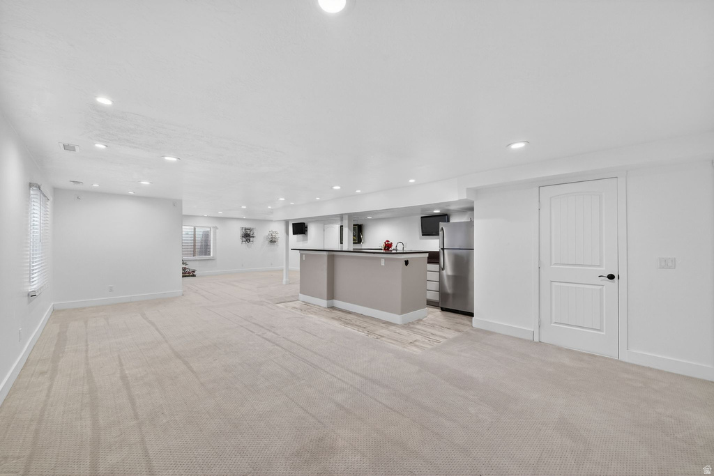Spacious finished lower level featuring recessed lighting, light-toned carpet, a built-in wet bar with a dark countertop, stainless steel refrigerator, and paneled interior doors