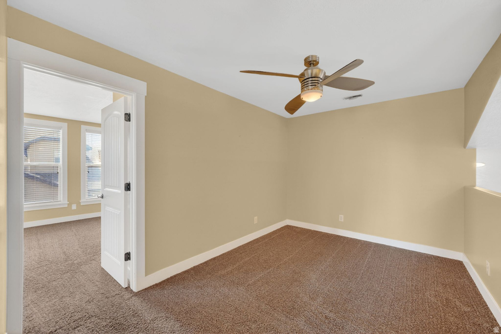Carpeted room featuring a ceiling fan with integrated lighting, a white paneled door with dark hardware, and light-toned walls