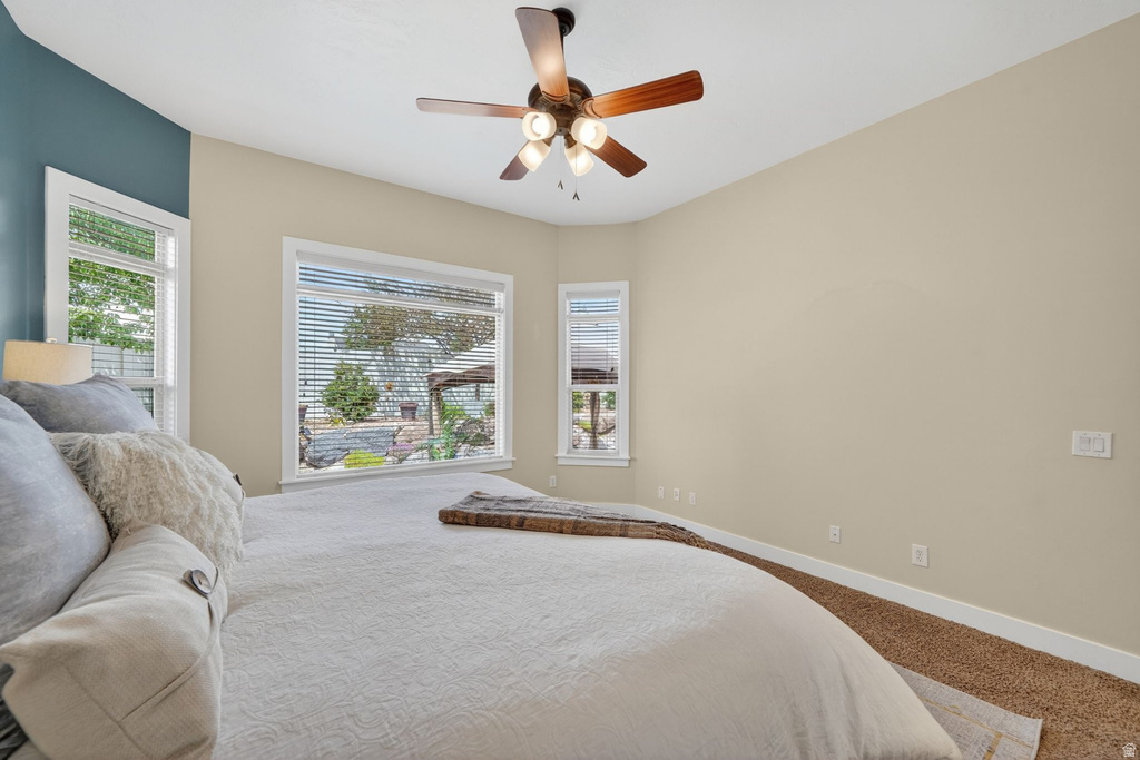 Bedroom featuring a ceiling fan with integrated lighting, multiple windows with blinds, a contrasting accent wall, and neutral-toned wall paint