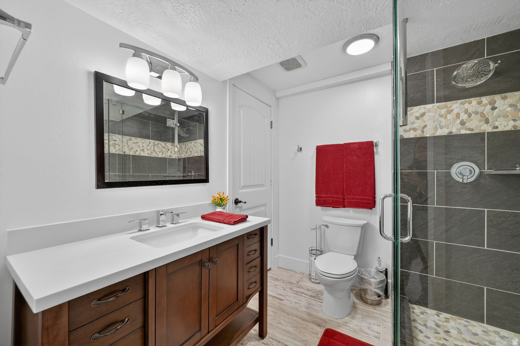 Bathroom featuring a glass-enclosed shower with slate-style and mosaic tile, a wood-finish vanity with an integrated sink, a solid surface countertop, and wood-finish flooring
