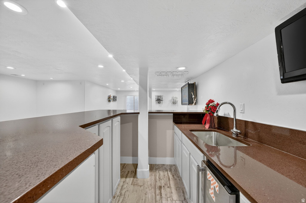 Full wet bar featuring a stainless steel sink, gooseneck faucet, light cabinetry, and rich countertop