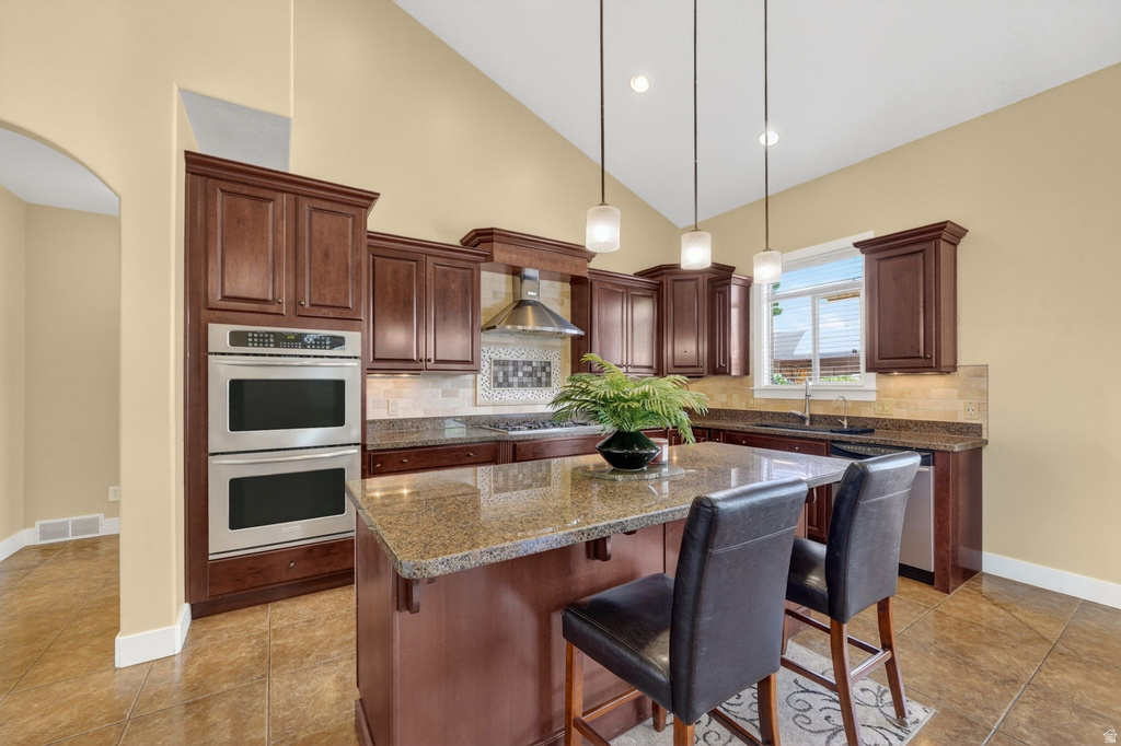 Kitchen featuring dark wood cabinetry, a central island with a stone countertop, dual stainless steel ovens, and tile flooring
