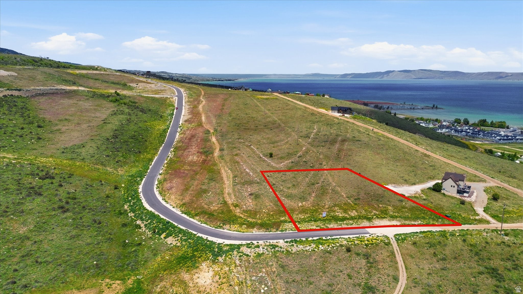 Expansive hillside parcel featuring a defined lot boundary, paved road frontage, and distant lake scenery