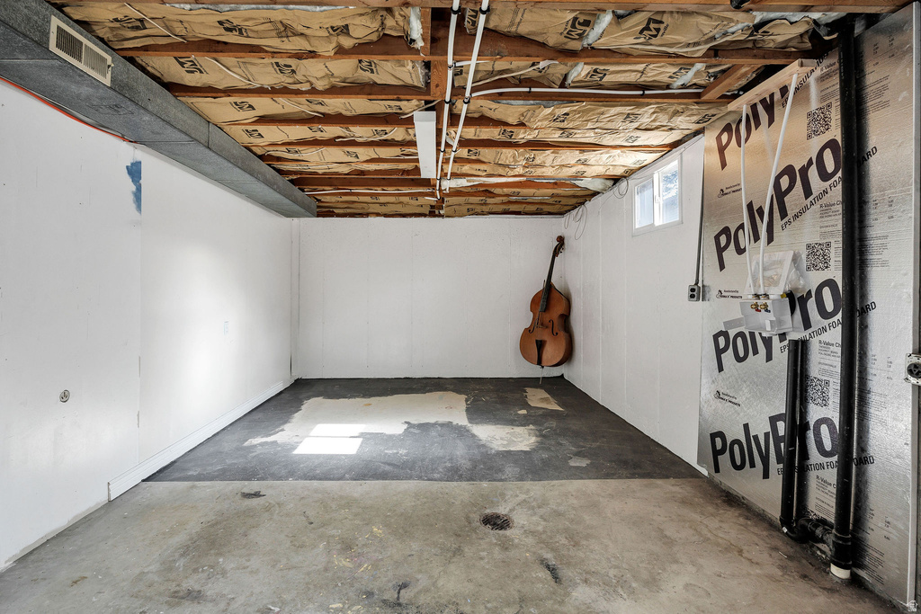 Unfinished basement space featuring exposed ceiling joists, insulation, and concrete flooring