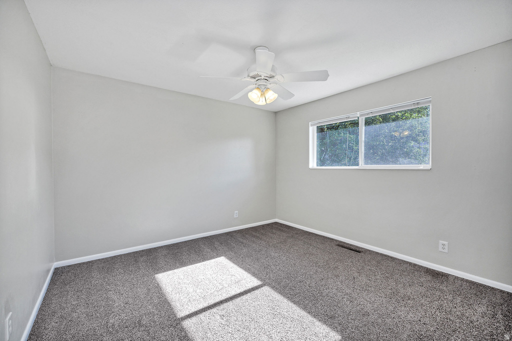 Carpeted interior space featuring light gray wall paint, white trim, and a ceiling fan with integrated lighting