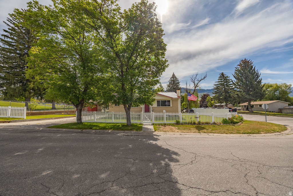 Corner lot property featuring a light-colored exterior, white picket fence, and mature trees