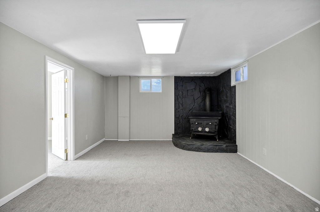 Spacious room featuring a corner wood-burning stove with a stone hearth, light gray walls, light gray carpeting, and a recessed ceiling light fixture