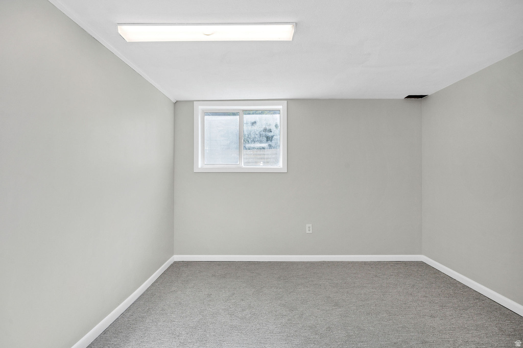 Room featuring gray wall paint, gray carpet flooring, a single window with white trim, white baseboards, and a fluorescent ceiling light fixture