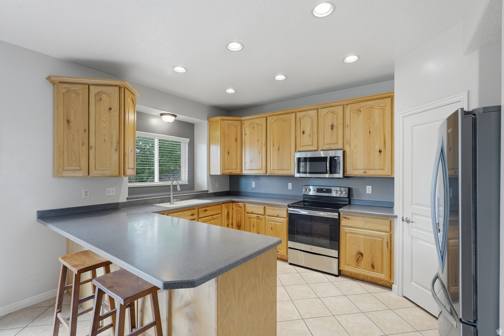 Kitchen featuring natural wood cabinetry, stainless steel appliances, a corner sink with a window, recessed lighting, and a breakfast bar with solid surface countertops