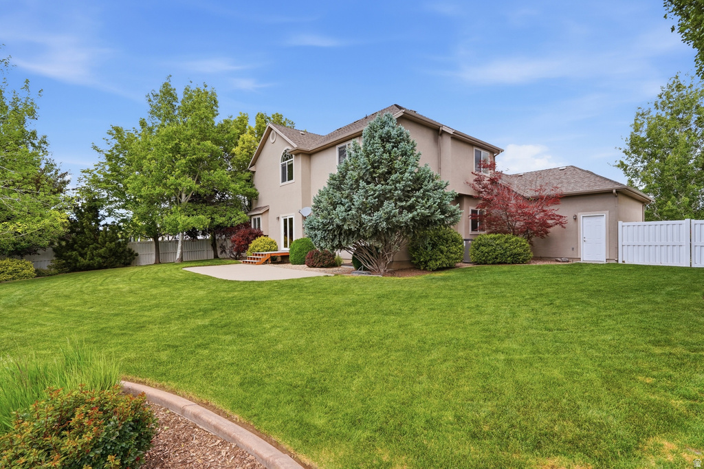 Expansive backyard featuring a large green lawn, concrete patio, mature trees, and a white privacy fence