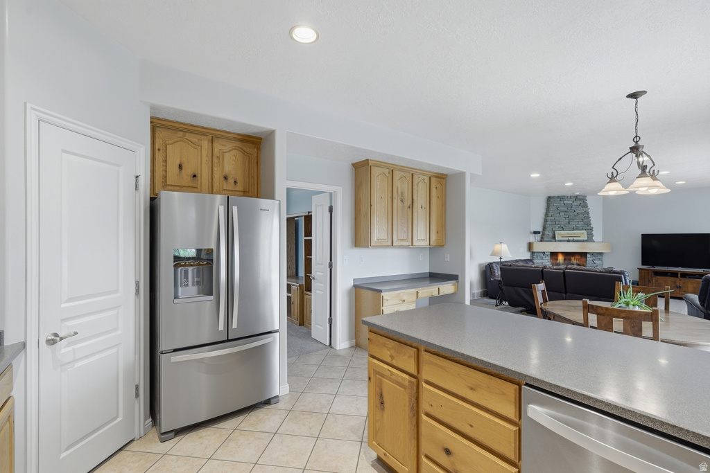 Open-concept kitchen and living area featuring a stone fireplace, light wood cabinetry, stainless steel appliances, and a large central island with a solid surface countertop