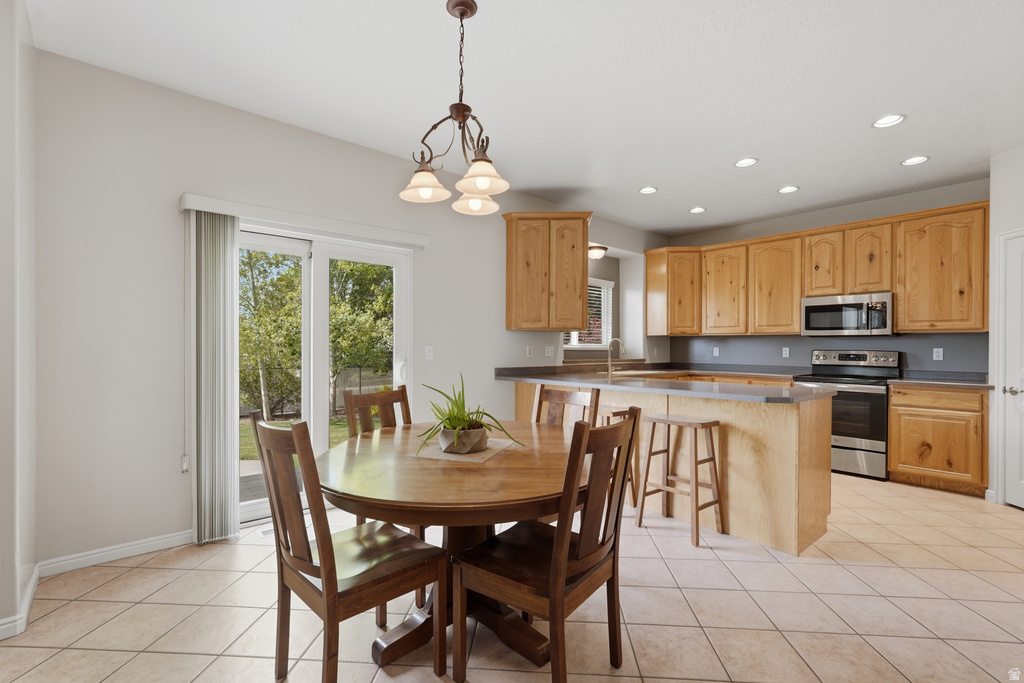 Kitchen and dining area featuring light wood cabinetry, stainless steel appliances, a center island with bar seating, tile flooring, and a sliding glass door