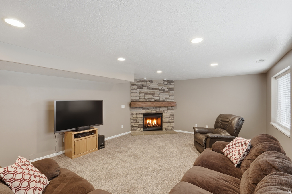 Spacious living area featuring a stone fireplace with a wood mantel, recessed lighting, neutral carpeting, and a window with blinds