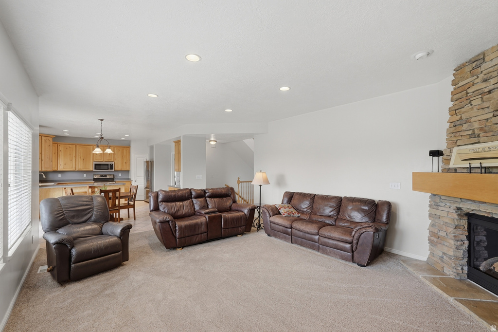 Spacious living area featuring a stacked stone fireplace with a wood mantel, recessed lighting, and light-toned carpeting