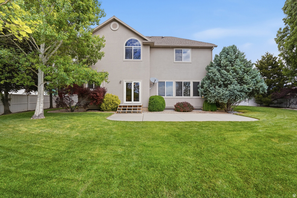 Expansive rear yard featuring a large concrete patio, mature trees, manicured lawn, and privacy fencing