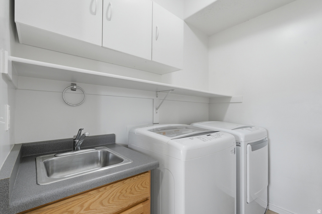Utility room featuring white cabinetry, a single-basin sink with a chrome faucet, a grey countertop, and wood-finish lower cabinetry