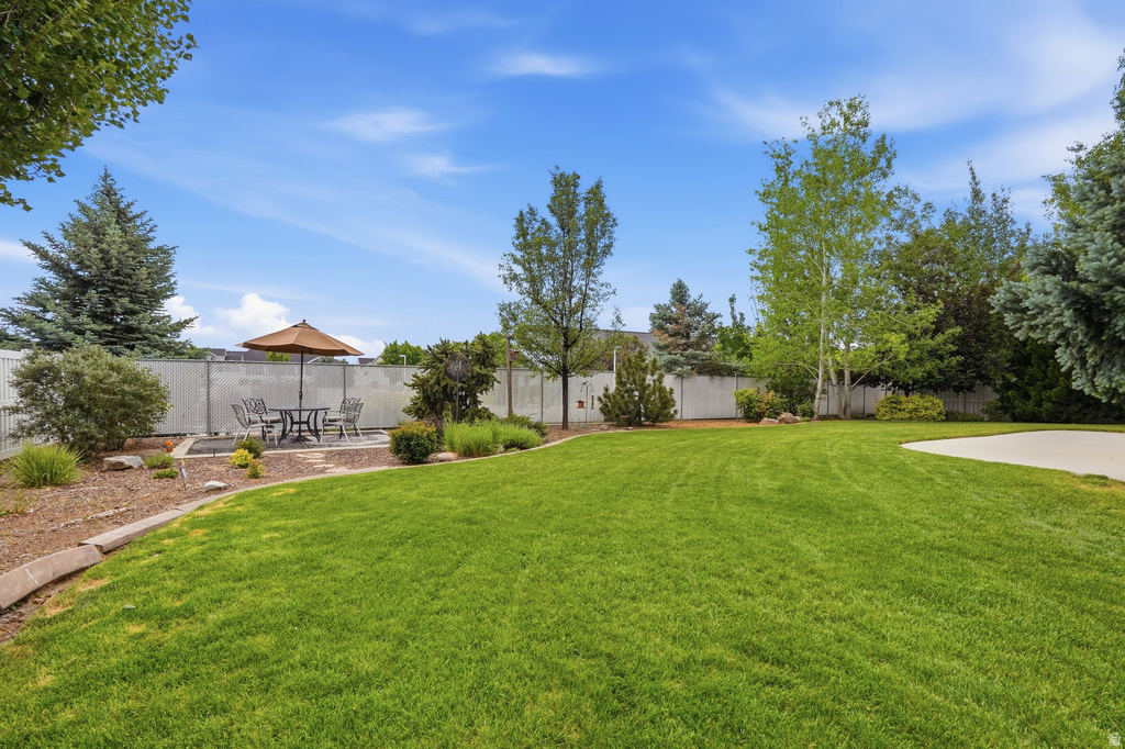 Expansive backyard featuring a lush lawn, concrete patio with paver accents, established landscaping beds, mature trees, and privacy fencing