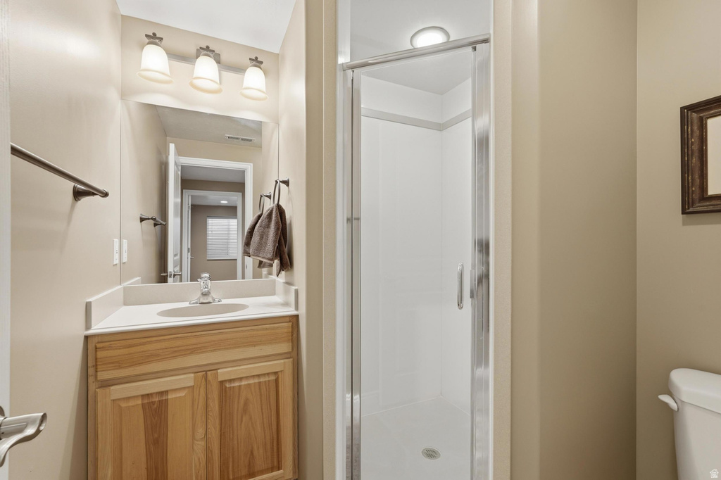 Bathroom featuring a glass-enclosed shower, a wood-finish vanity with a built-in sink, a wall-mounted mirror, and a three-light vanity fixture